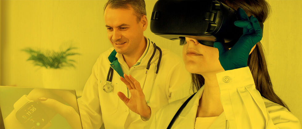 Médico sentado à mesa com portátil à sua frente acena para o portátil, demonstrando uso de tecnologia em teleconsulta, e médica com óculos de realidade virtual ao lado, ilustração sobreposta ao portátil de uma relógio digital com dados de saúde